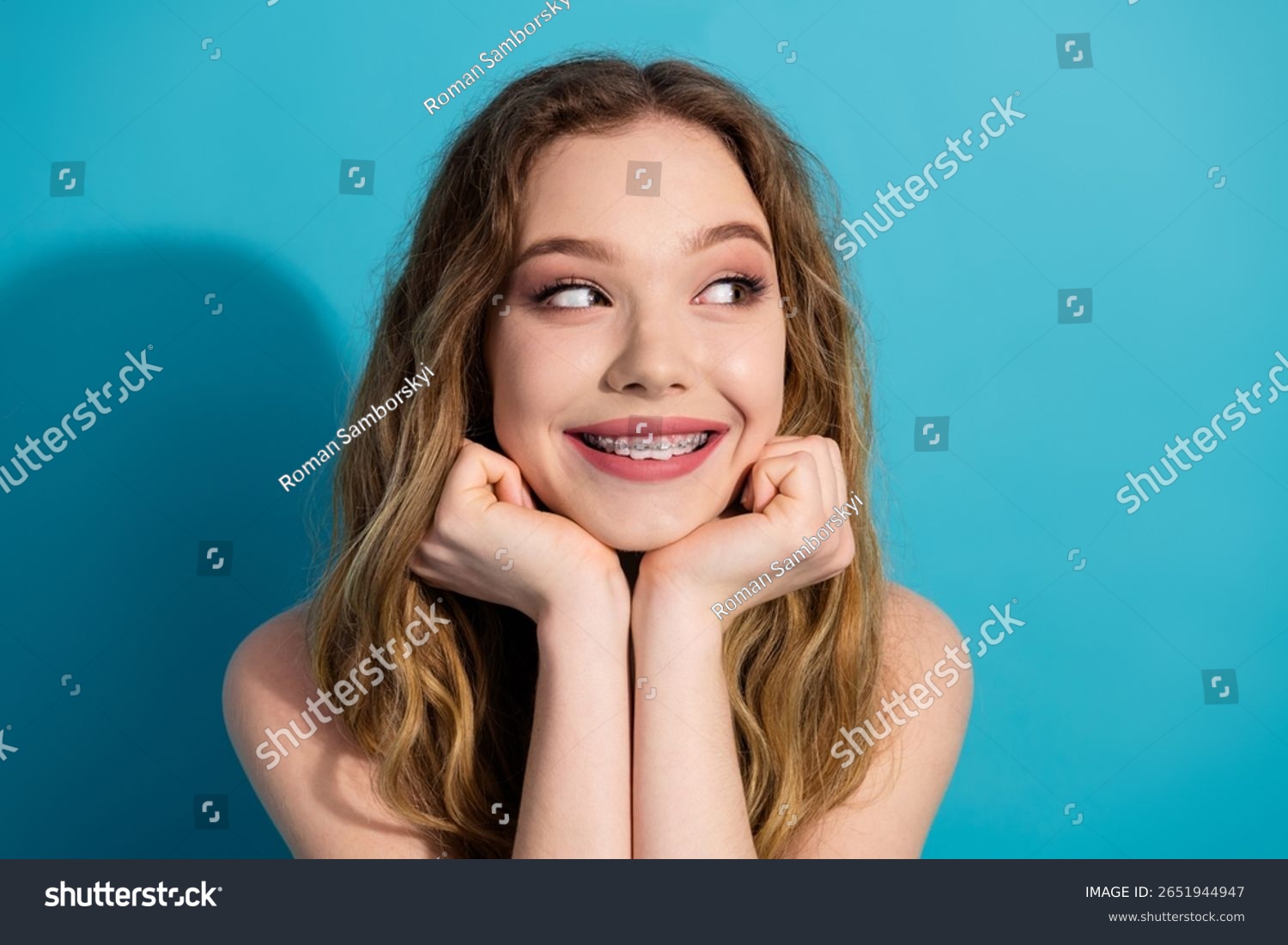 stock-photo-smiling-pretty-young-woman-with-braces-resting-hands-on-face-against-vibrant-blue-background-2651944947